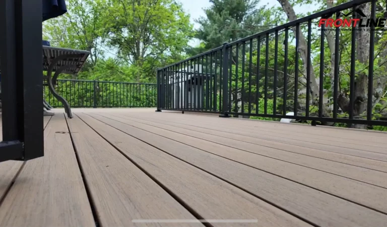 A close-up view of a wooden deck with a black railing, surrounded by lush greenery and trees in the background, highlighting a serene outdoor space.