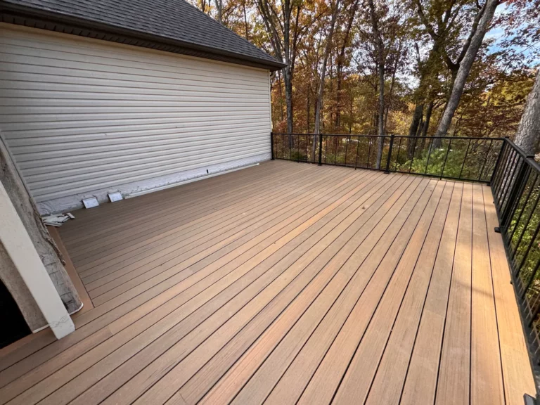 A spacious wooden deck with a modern design, surrounded by trees with autumn foliage, creating a peaceful outdoor space.